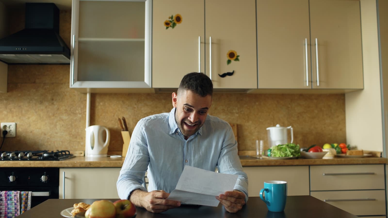 Person reading a letter at a kitchen table with papers spread out