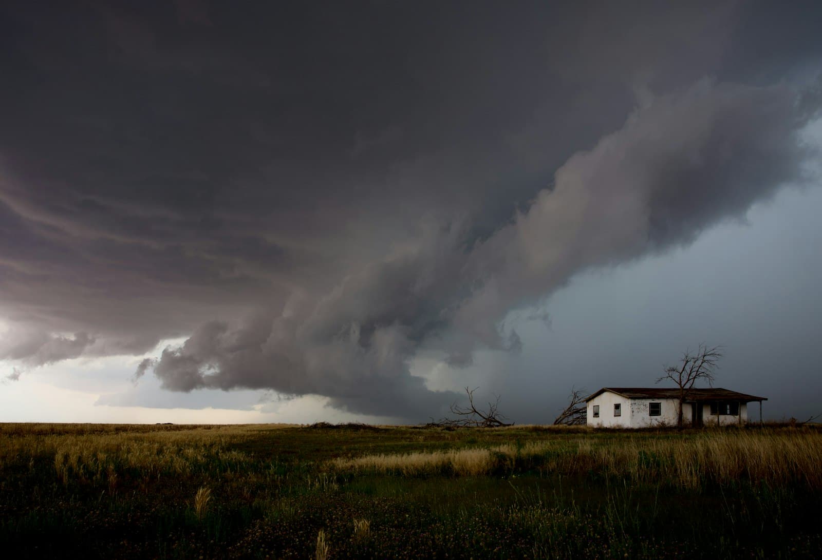 Dark storm clouds advancing over a small house on a flat landscape